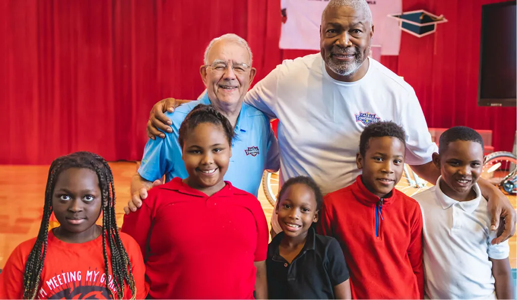 Tackle Tomorrow volunteers with students in front of a red backdrop